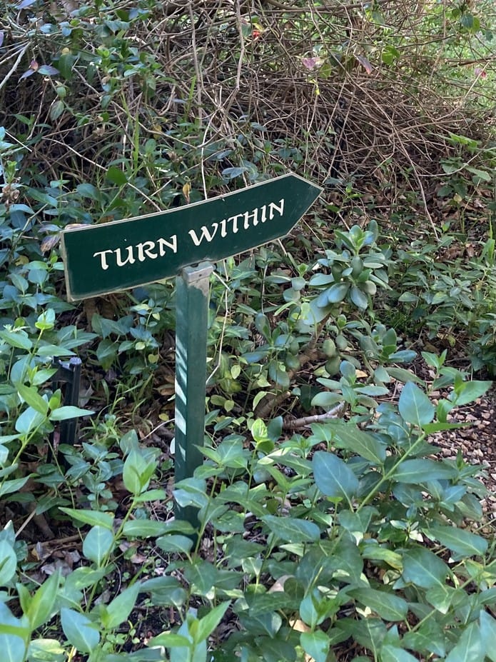A hand-painted garden sign pointing along a path: Turn within